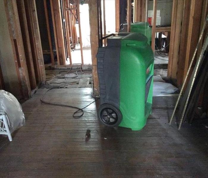 green device on hardwood floor, some removed, bare studs for walls