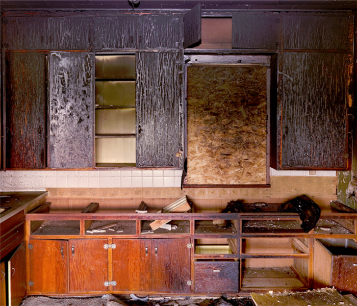 a fire damaged kitchen with soot covering the cabinets and walls and debris everywhere