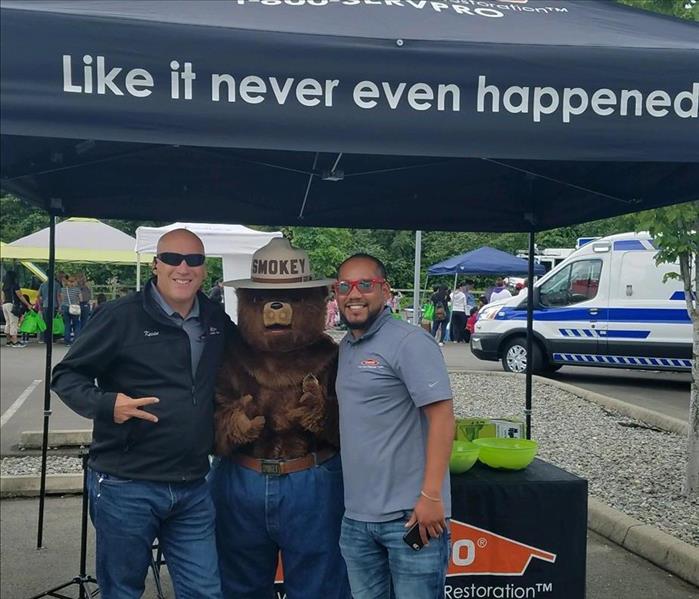 two male employees standing with Smokey the bear under a black SERVPRO tent